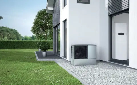 Unità esterna per riscaldamento con condizionatore, posizionata accanto a una casa moderna con giardino curato.