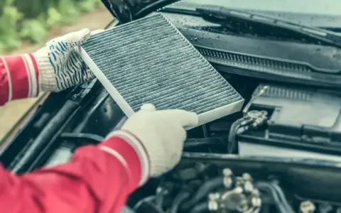 Hands in gloves hold a dirty cabin air filter, ready for replacement. This contrasts with the engine air filter, unseen but vital for car performance.