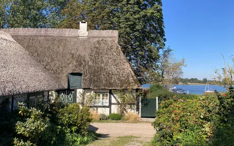 Reetgedecktes Haus am Wasser, ein **damp geheimtipp** mit Booten im Hintergrund.