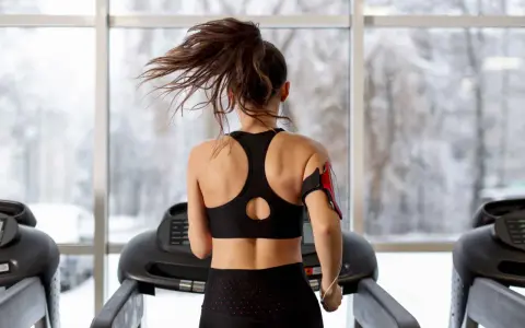 Une femme fait du sport à jeun sur un tapis roulant, ses cheveux flottant au vent. Dehors, la neige tombe.