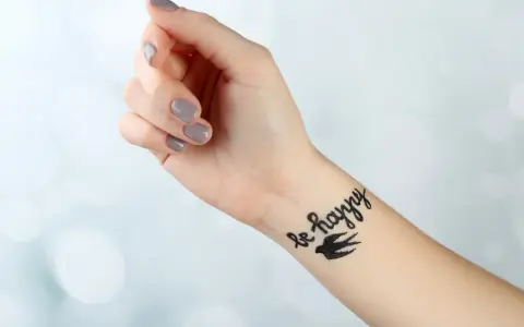 Dłoń z tatuażem "be happy" i ptakiem. Pielęgnacja tatuażu: jak długo smarować, by był piękny.