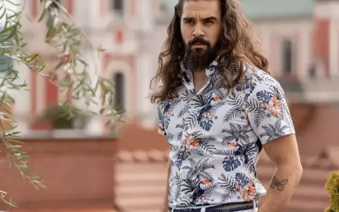 Mężczyzna z długimi włosami w hawajskiej koszuli na t-shirt, z motywem liści i ptaków.