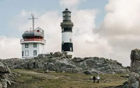 Deux phares se dressent sur une côte rocheuse à Ouessant. Que faire ? Se promener et admirer le paysage, comme ces deux randonneurs.