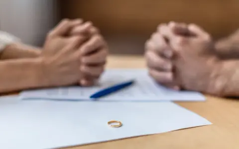 Złożone dłonie nad dokumentami, na stole leży obrączka. Czas na decyzję o zmianie nazwiska rodowego.