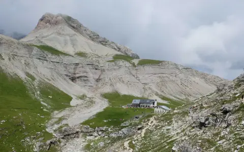 Rifugio alpino con escursionisti e gregge in un paesaggio montano mozzafiato, vicino a Passo Val Gardena.