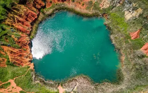 Lago turchese circondato da rocce rosse e vegetazione rigogliosa, un paesaggio suggestivo che ricorda le cave di bauxite.