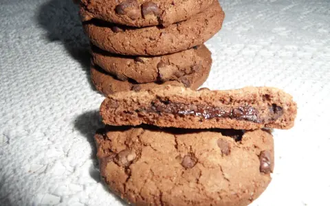 Gros plan sur une pile de biscuits au chocolat, dont un est coupé en deux révélant un cœur coulant de Nutella. Une recette de biscuit Nutella parfaite pour les gourmands.