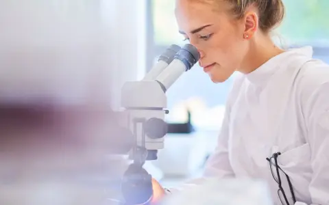 Ricerca scientifica per capire cos'è il sarcoma. Giovane scienziata al microscopio.