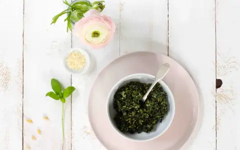 Schüssel mit frischem Basilikum-Pesto, Pinienkernen, Parmesan und einer zarten rosa Blume. Ein Hauch des originalrezepts.