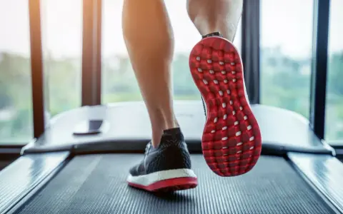 Gambe che corrono su un tapis roulant, con una scarpa rossa e nera in primo piano. Un'ottima immagine per chi vuole capire come iniziare a camminare.