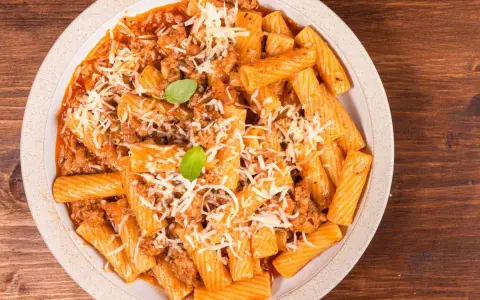 Un piatto invitante di pasta alla zozzona, con rigatoni conditi con un ricco ragù e abbondante parmigiano grattugiato, guarnito con basilico fresco.