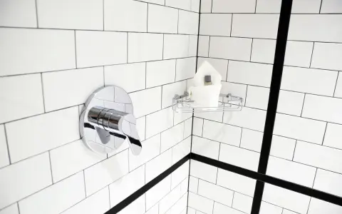 Un robinet de douche chromé et une étagère avec des serviettes sur un mur de carrelage blanc. Idéal pour nettoyer carrelage mural encrassé.