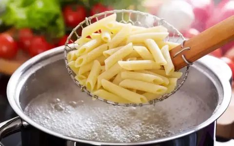 Gotowanie penne do pysznych dań z makaronem. W tle pomidory i sałata.