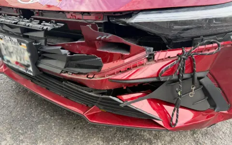 A red car's front bumper is severely damaged, with broken plastic and a rope tied to it. This damage might be from hail, and the owner is likely wondering how do you repair hail damage on a car.
