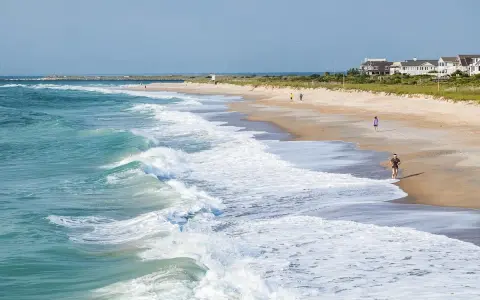 Waves crash on the shore at Wrightsville Beach, where people enjoy a run and a stroll, showcasing some of the relaxing things to do.