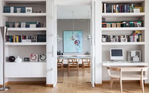 Ampia libreria in cartongesso con libri, computer e decorazioni. Si intravede una sala da pranzo con un quadro astratto.