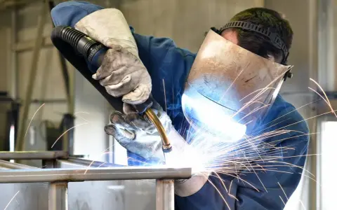 Soldador con máscara y guantes, demostrando cómo soldar con electrodo, creando chispas brillantes.