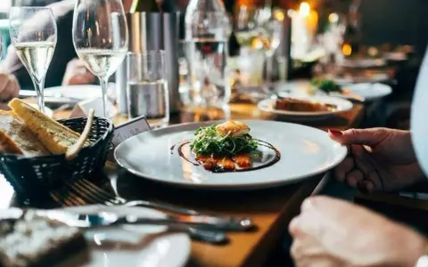 Une assiette de saumon avec garniture verte, du pain dans un panier, des verres de vin et des bougies allumées. Bon appétit !