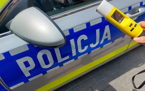 Policjantka trzyma alkomat przy radiowozie. Wynik 13.7 promila to nierealny, ale symboliczny wynik dla kierowcy pod wpływem alkoholu.