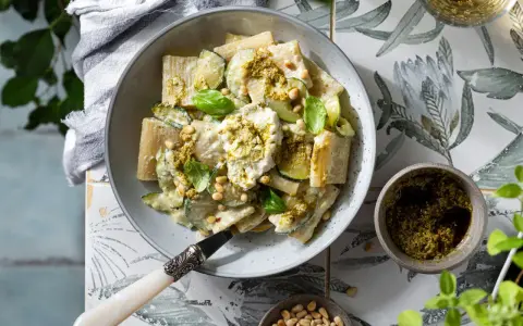 Piatto di pasta ricotta e zucchine, condito con pesto e pinoli, guarnito con basilico fresco.