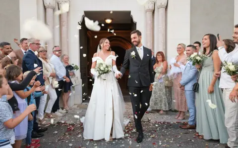 Photographie de mariage : le couple sort de l'église sous une pluie de pétales, entouré de leurs invités joyeux.