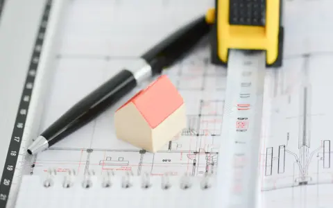 Model domu, długopis i miarka na planach architektonicznych. Pokazuje, ile jest ważne pozwolenie na budowę.