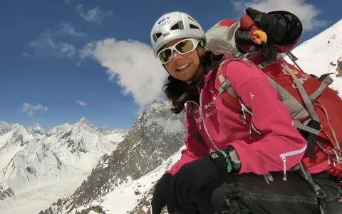 Gerlinde Kaltenbrunner, lächelnd in voller Bergsteigerausrüstung, vor einer majestätischen Schneelandschaft.