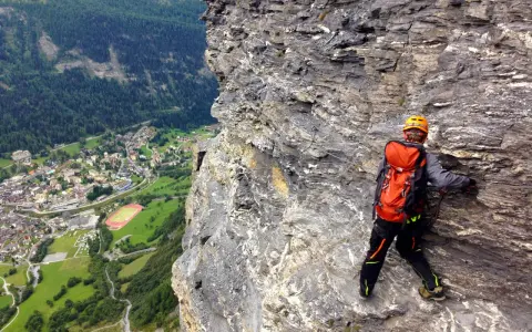 Wspinaczka via ferrata w Szwajcarii. Widok na dolinę i miasteczko z perspektywy skalnej ściany.