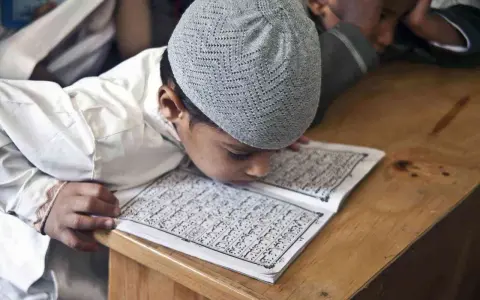 Chłopiec w czapce na głowie pochyla się nad Kor'anem, ucząc się o senegalskiej religii.
