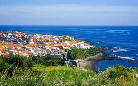 Malownicze miasteczko na wybrzeżu Portugalii, z białymi domami i pomarańczowymi dachami, nad błękitnym oceanem. Ceny wakacji w Portugalii mogą być zaskakująco przystępne.
