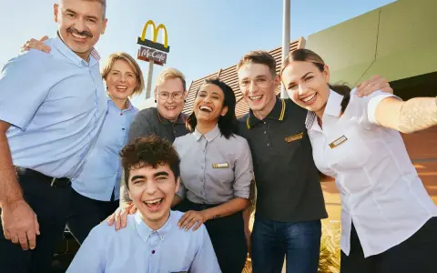 Uśmiechnięty zespół McDonald's, gotowy do pracy. W tle logo McCafe.