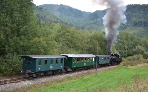 Dampflok der slowakischen Bahn fährt durch eine grüne Landschaft.