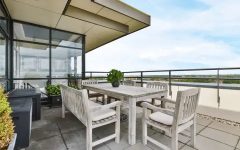 Mesa de madera y sillas en una terraza con vistas al cielo azul.