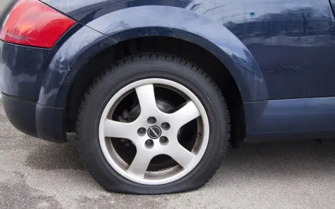Ruota posteriore di un'auto blu con evidente perdita pressione pneumatici. Il pneumatico è sgonfio e appoggiato a terra.