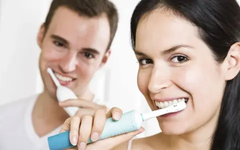 Para jak myć zęby szczoteczką soniczną, uśmiechając się do kamery.