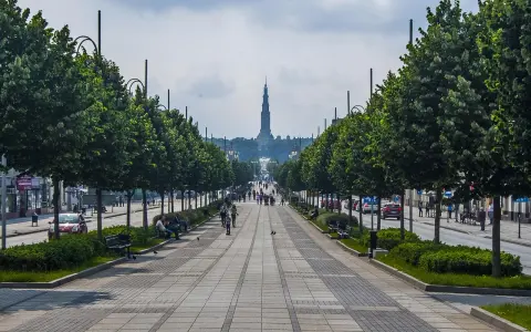 Aleja z drzewami i ławkami prowadzi do Jasnej Góry. Spacerowicze i samochody na ulicy. Co na mieście Częstochowa?