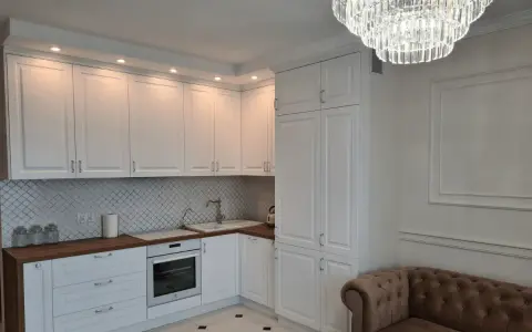 Elegancka kuchnia w stylu angielskim z białymi frontami, drewnianym blatem i kryształowym żyrandolem.
