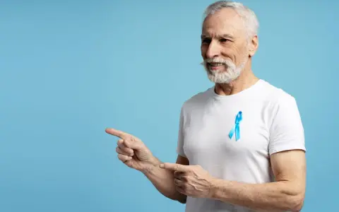 Starszy pan z niebieską wstążką na piersi, wskazujący palcami w lewo. To symbol walki z rakiem prostaty, ważnym tematem dla każdego psa 8.