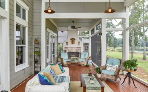 A cozy screened-in patio with a fireplace, wicker chairs, and a sofa, perfect for enjoying the view of the lake.