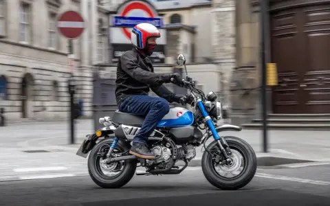 Mężczyzna w kasku jedzie na małym motocyklu, przypominającym boda boda, po ulicy miasta.
