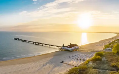 Sonnenuntergang am Ostsee Strand mit langer Seebrücke und Strandkörben.