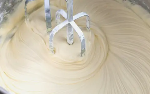 Mieszadła miksera zagłębiają się w puszysty krem z mascarpone i białej czekolady, tworząc faliste wzory.