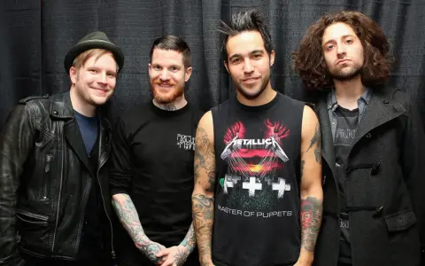 Czterech mężczyzn z zespołu Fall Out Boy pozuje do zdjęcia na tle czarnej kurtyny.