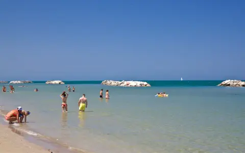 Persone si godono una giornata di sole sulla spiaggia libera di Torre Pedrera, tra bagni e relax in mare.