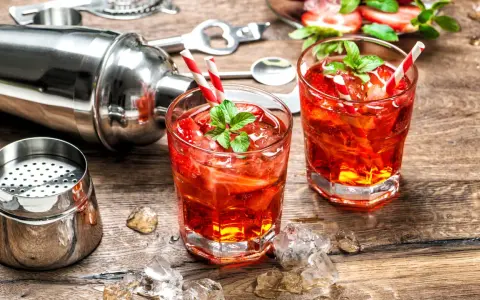 Zwei erfrischende Erdbeer-Cocktails mit Minze und Eiswürfeln, bereit zum Genießen. Ein Shaker und Bar-Werkzeuge deuten auf das kunstvolle Alkohol mischen hin.