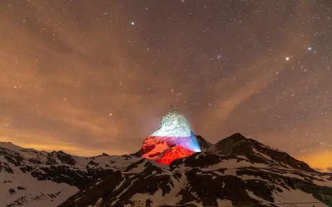 Górski szczyt, niczym polski Matterhorn, rozświetlony nocą polskimi barwami pod rozgwieżdżonym niebem.