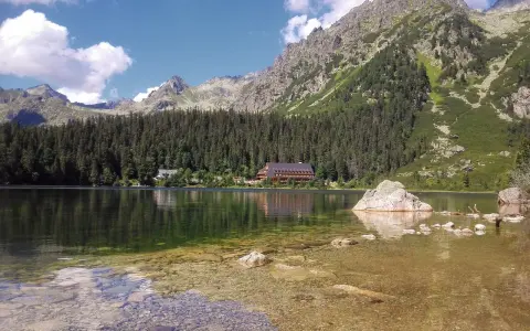 Spokojne Popradske Pleso odbija góry i las. Kamienie w płytkiej wodzie tworzą ścieżkę.