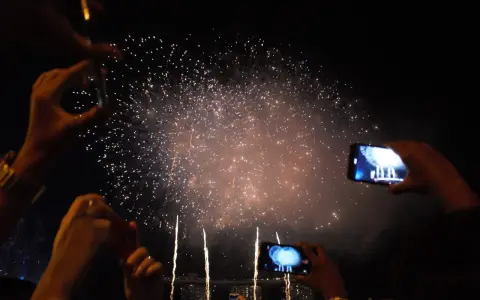 Des mains filment un magnifique feu d'artifice dans le ciel nocturne, capturant la magie de l'instant.