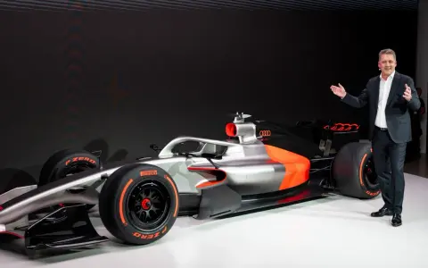 Ein Mann präsentiert stolz ein futuristisches Formel 1 Auto in Silber und Orange.