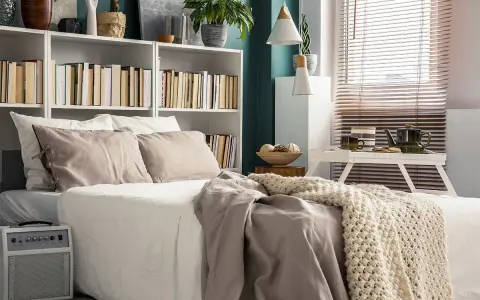 Una cama acogedora con una estantería encima llena de libros y plantas.